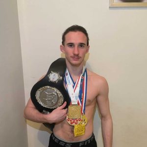 Un élève portant fièrement la ceinture de victoire de boxe sur son épaule, avec des médailles accrochées.